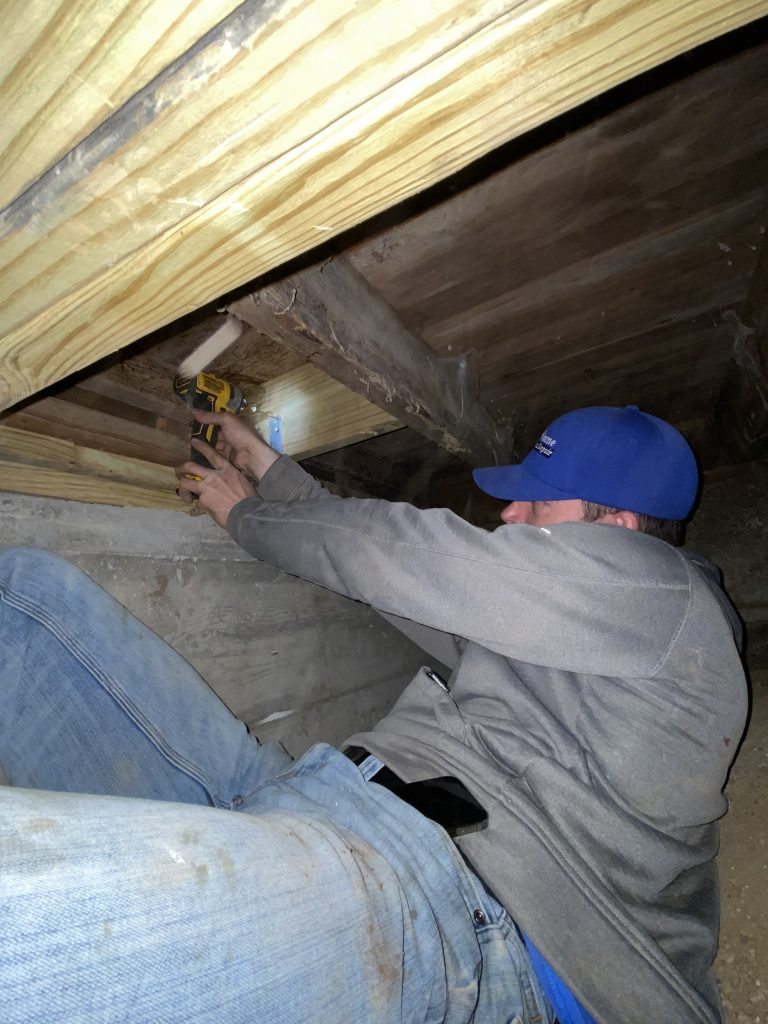 Crawl space foundation repair technician working under a Tulsa home