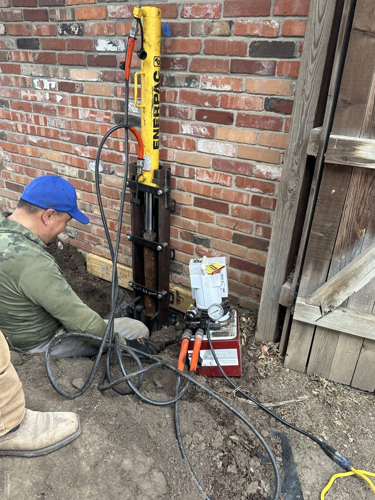 Level Home Foundation Repair crew installing eccentric steel pier bracket on residential foundation in Tulsa Oklahoma