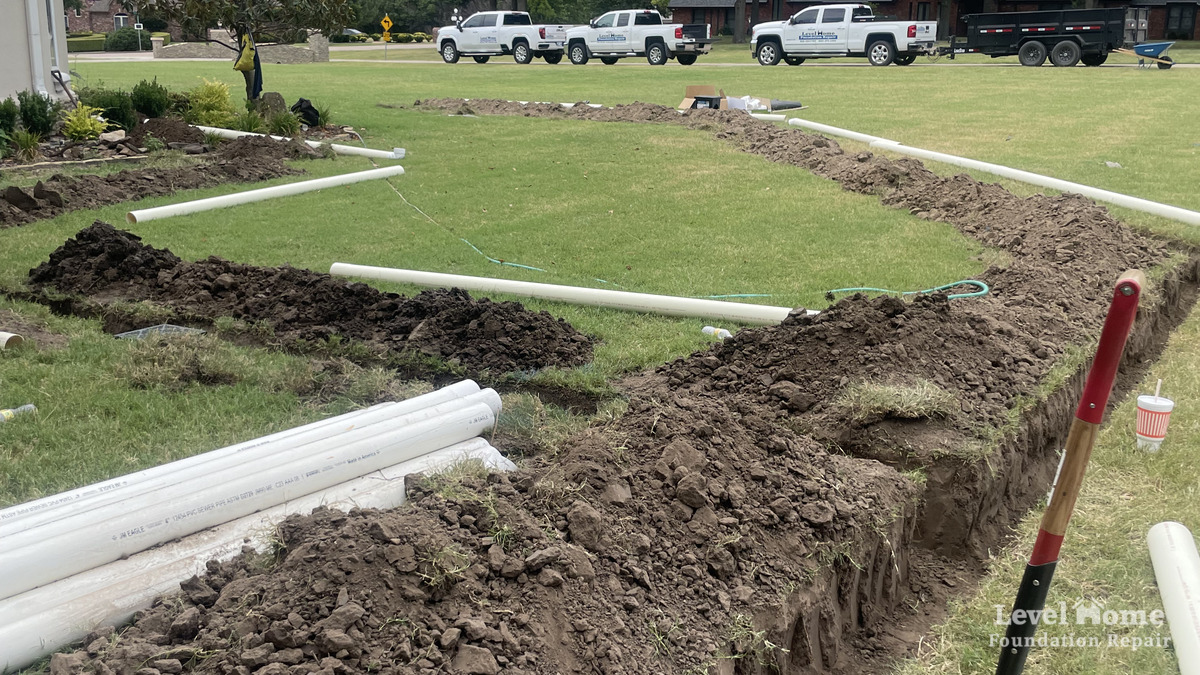 Level Home Foundation Repair crew installing tight-line PVC drainage system in residential yard Tulsa Oklahoma