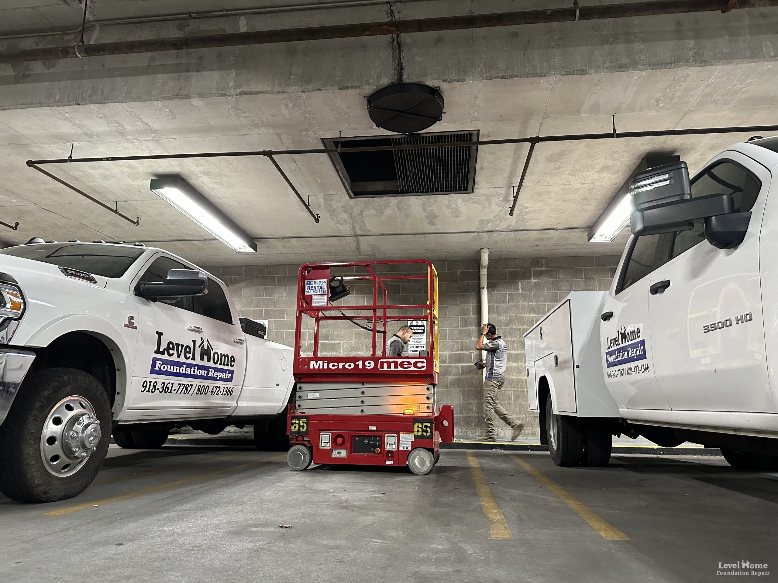 Level Home Foundation Repair fleet trucks and scissor lift staged inside a multi-story commercial parking garage