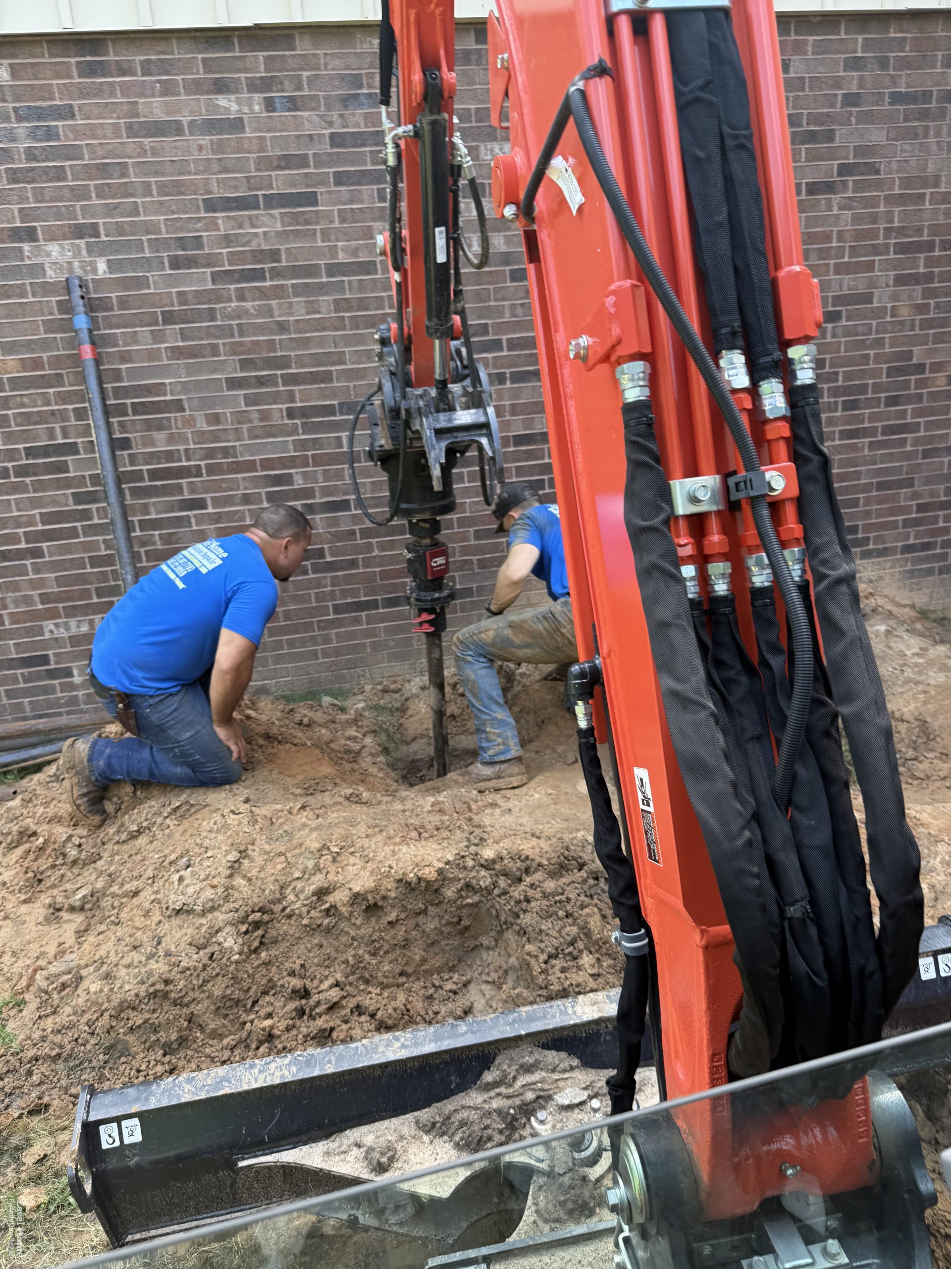 Helical pier installation with an excavator at a commercial building site in Tulsa Oklahoma