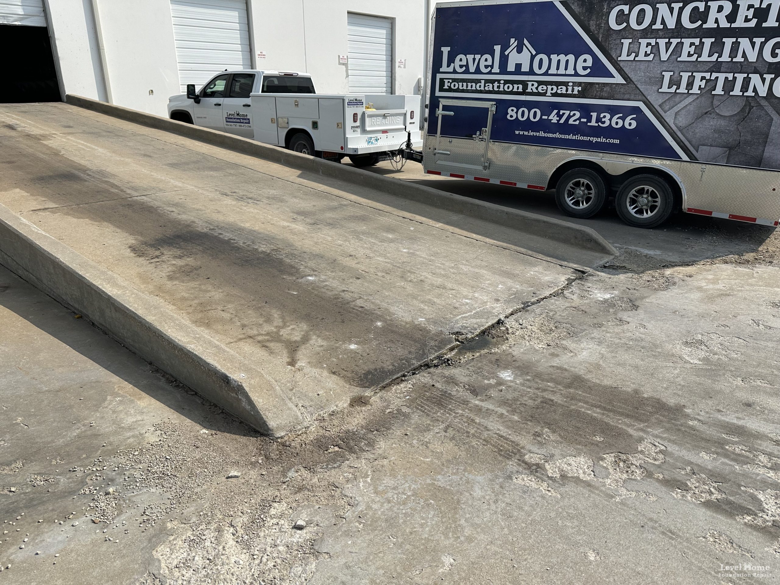 Loading dock concrete settlement repair with Level Home fleet vehicles staged at a commercial facility