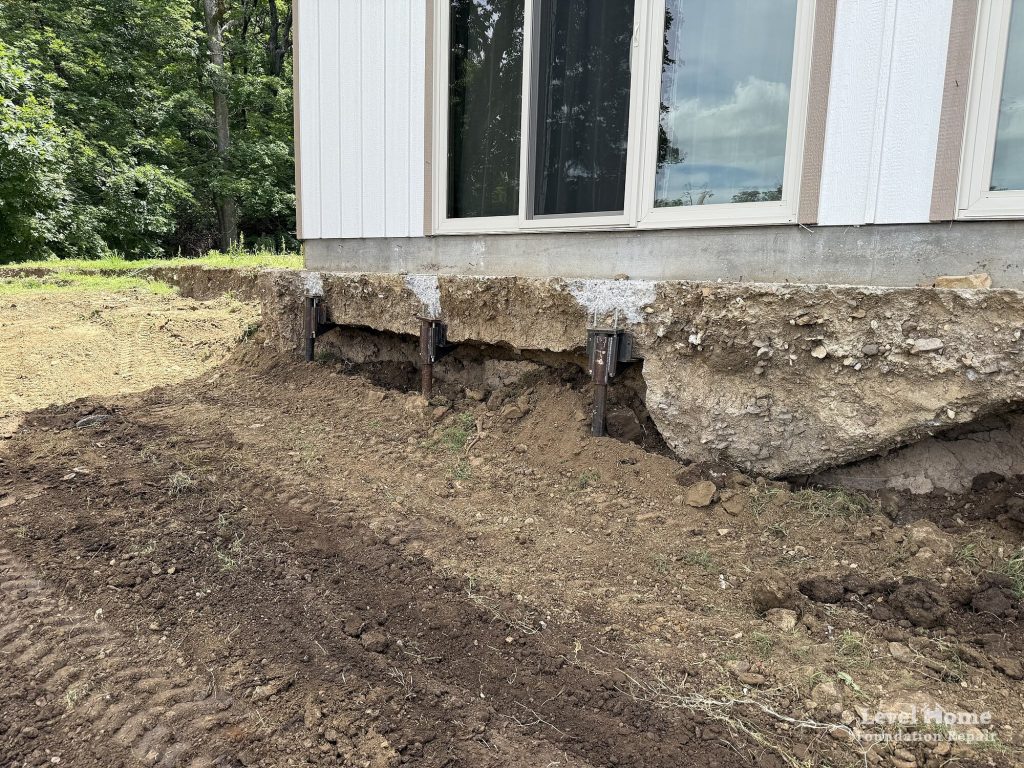 Exterior steel piers installed under the front footing of a Cookson, Oklahoma home after a hillside soil failure eroded the soil and left the foundation unsupported, foundation erosion repair by Level Home Foundation Repair