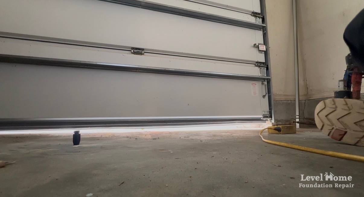 Before photo from floor level inside a garage showing a bright band of daylight under the closed garage door where the slab had settled