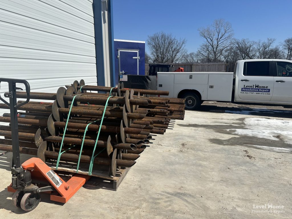 Pallet of steel helical piers with welded helix plates, strapped and ready for a new home foundation, with a Level Home Foundation Repair truck behind it